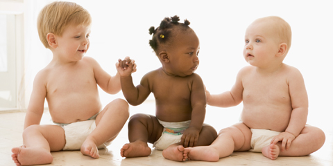 Three babies sitting indoors holding hands